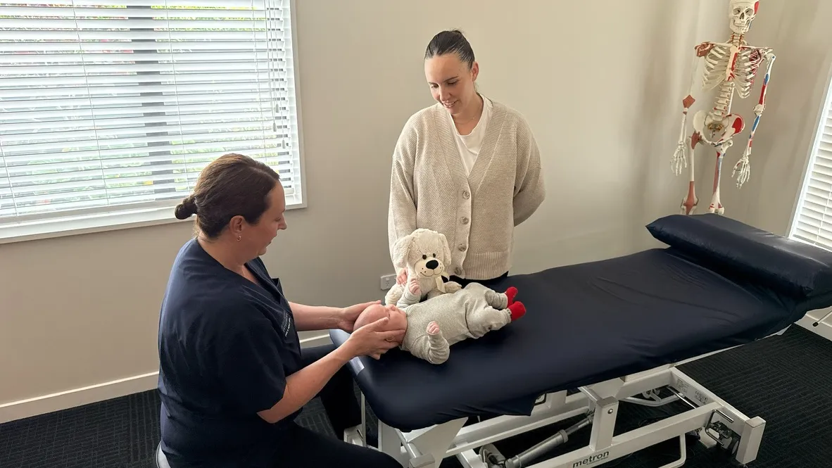 Lorraine Herity performing a paediatric osteopathic assessment on an infant, with the parent observing alongside