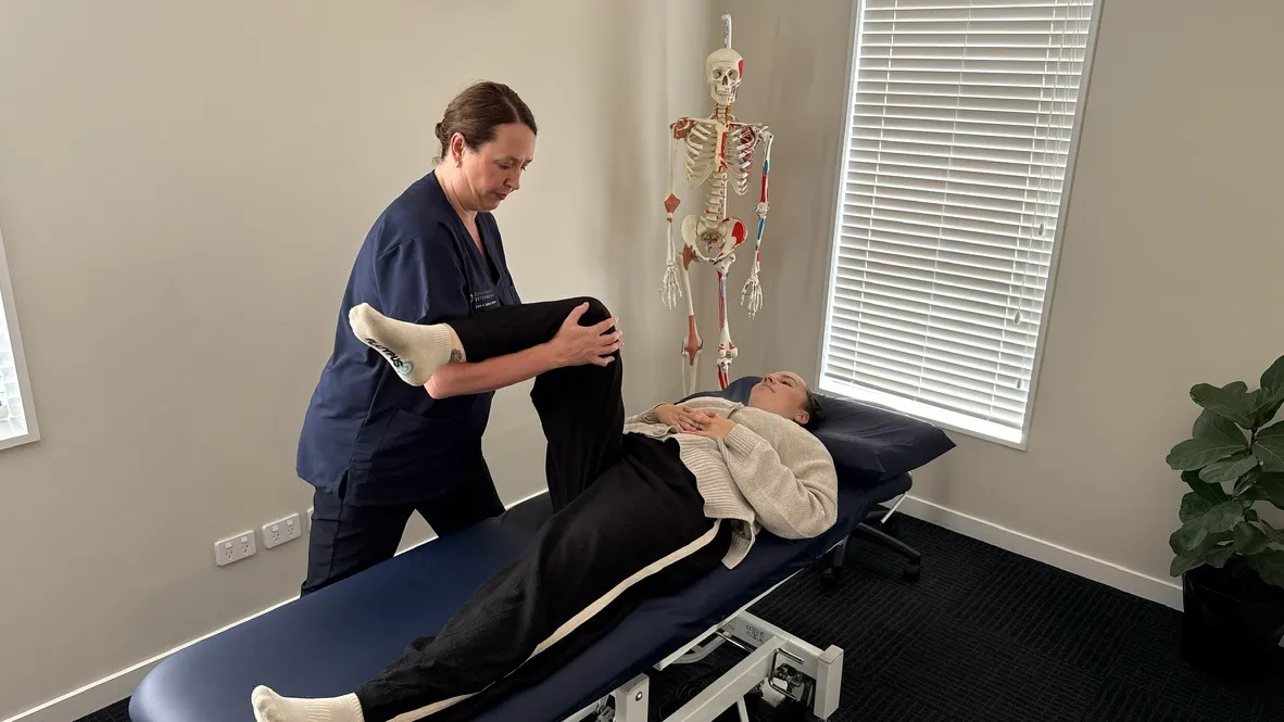 Lorraine Herity treating an adult female patient on a treatment bench with the anatomical reference visible behind